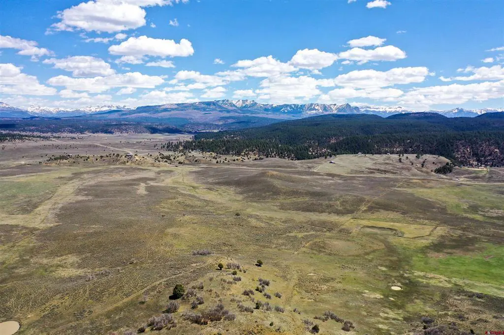 Aerial view of a large, grassy field with mountains in the background under a blue sky with white clouds.