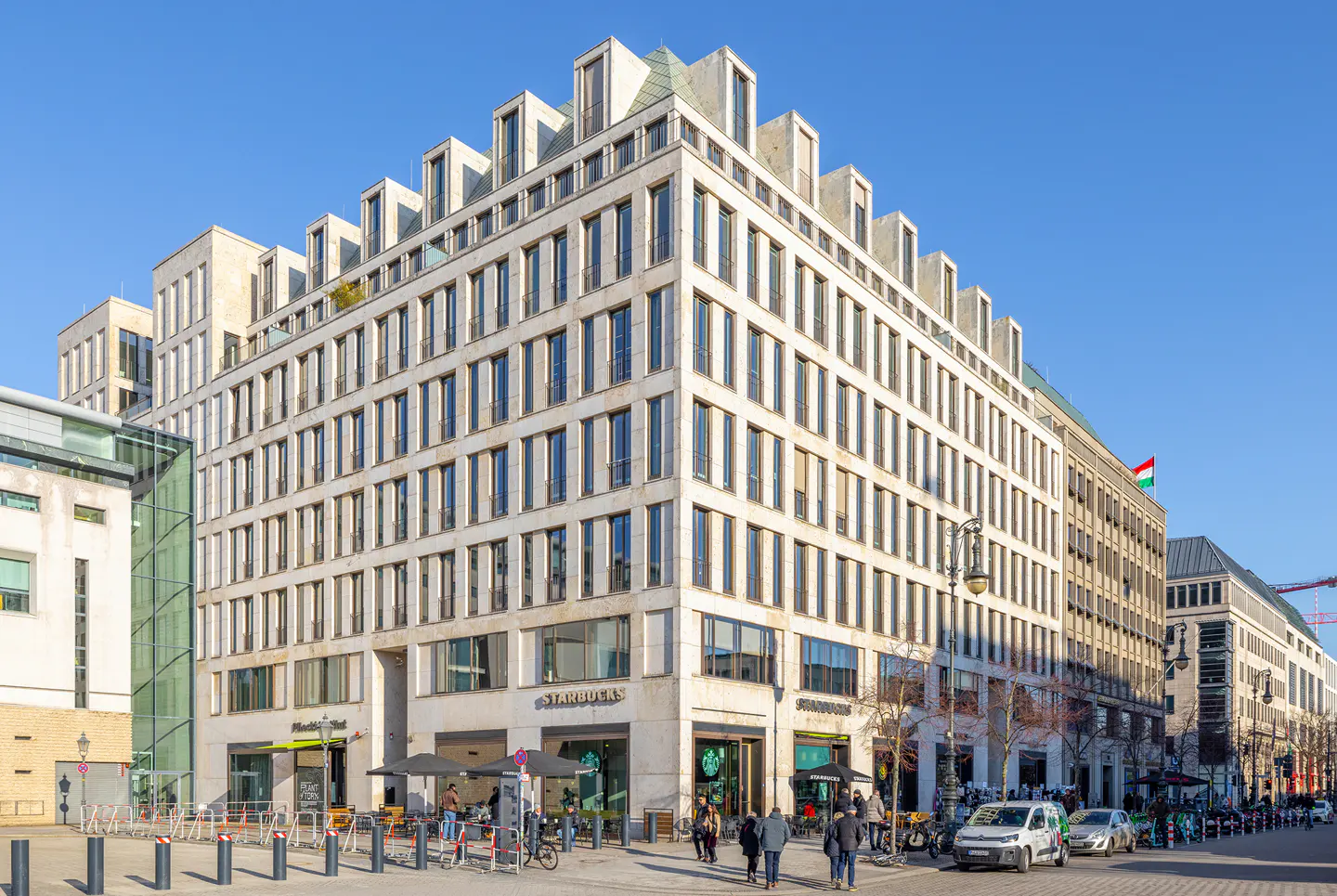 A multi-story building with a Starbucks on the ground floor, people walking on the sidewalk, and cars parked on the street.