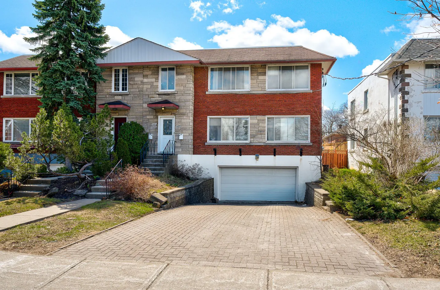 Exterior of a two-story townhouse with a brick and stone facade, a paved driveway, and a built-in garage.