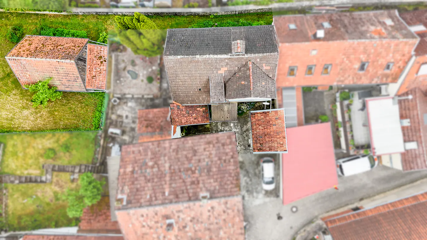 Aerial view of European houses with red tile roofs, green lawns, and a white car parked in a courtyard.