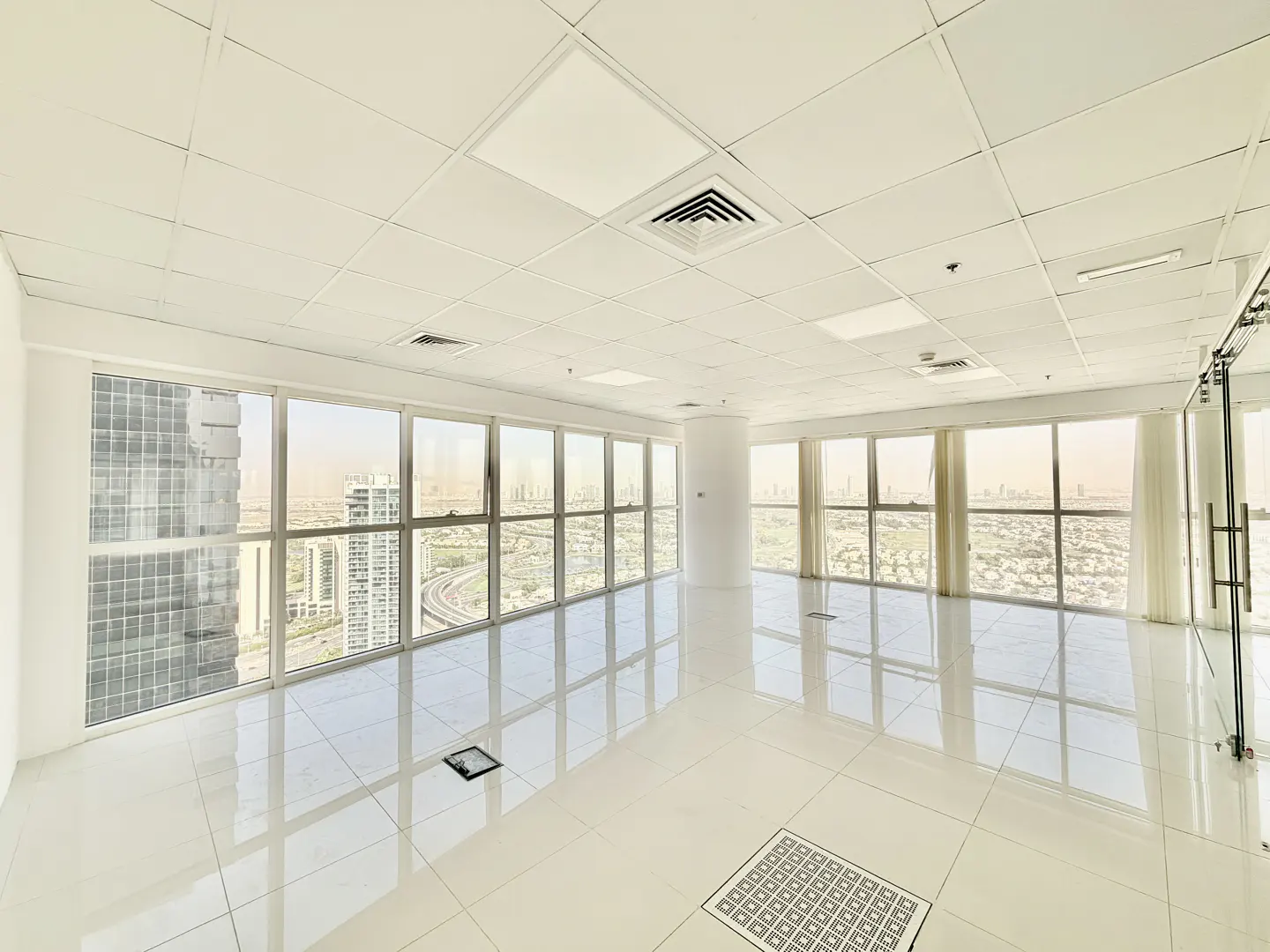 Bright, empty office space with white tile floors and large windows showing a city view.