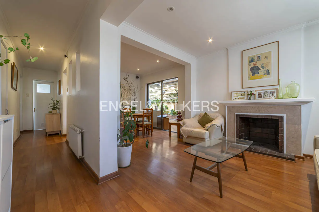 A bright living room with hardwood floors, a fireplace, and a glass coffee table. A dining area is visible through an archway.