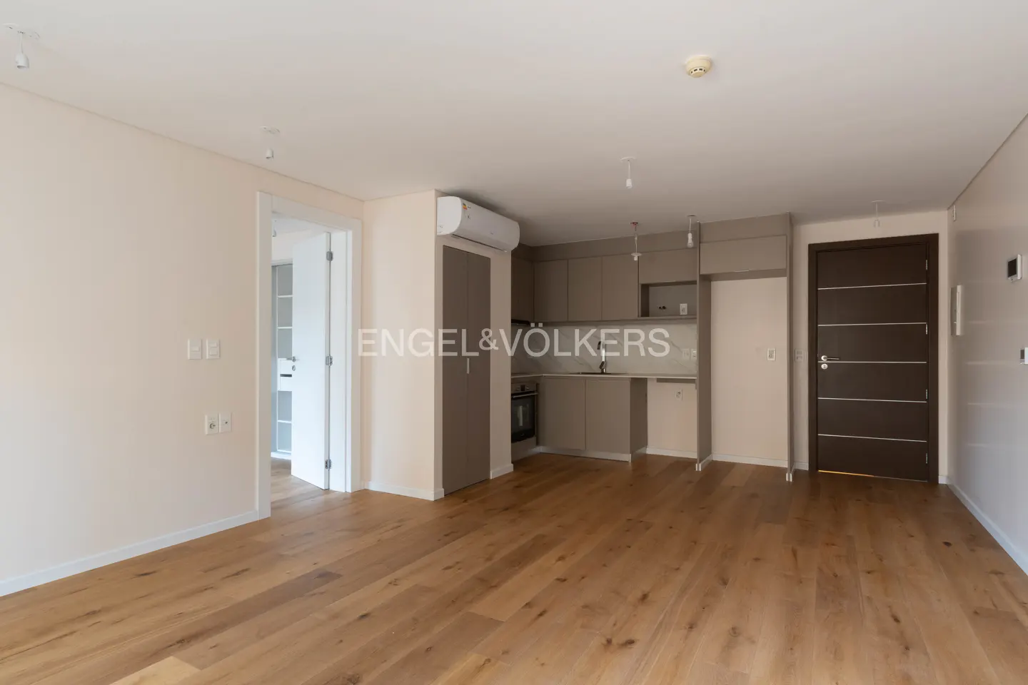 A bright, open-concept apartment with light wood floors, a gray kitchen, and white walls.
