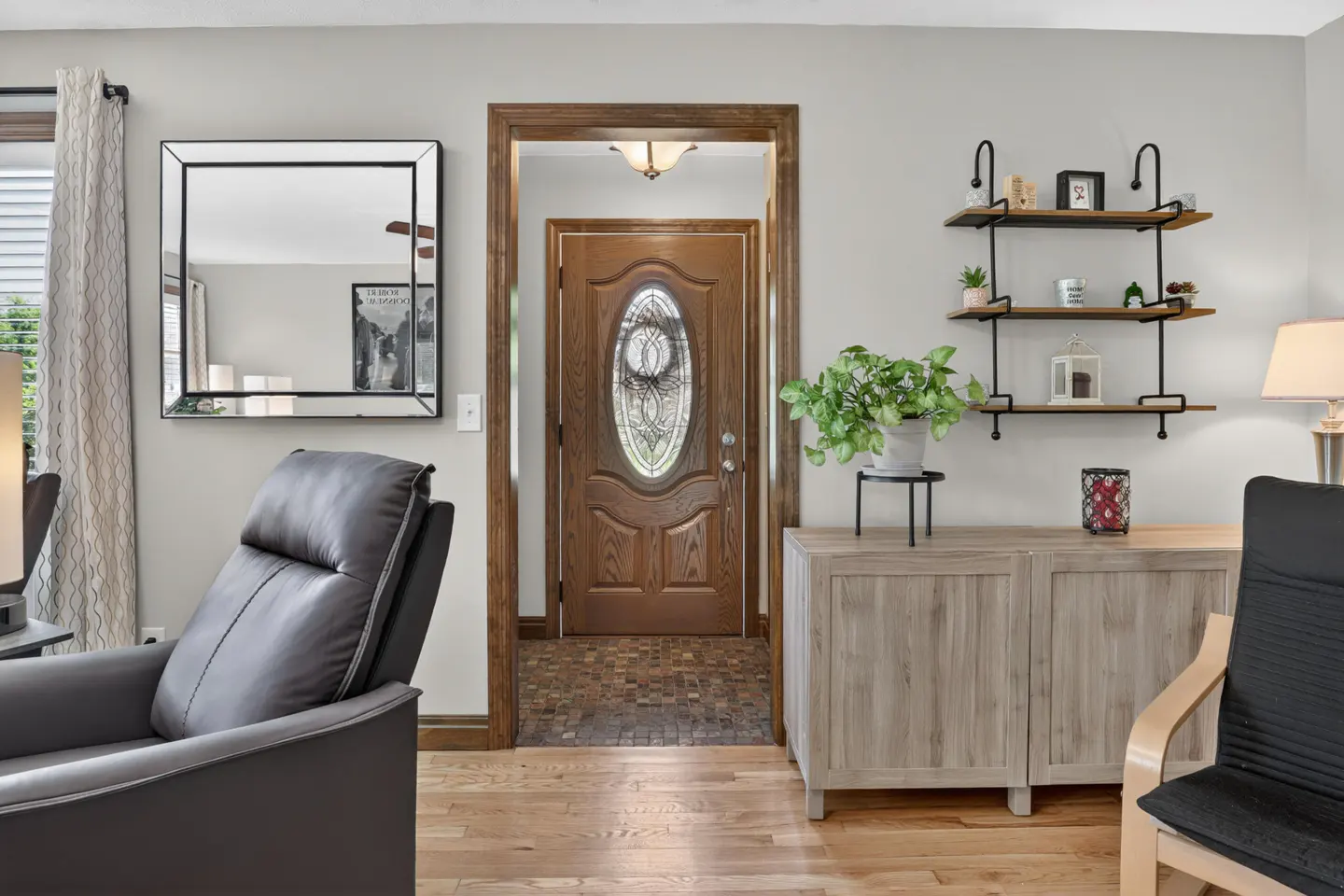 Living room view with a brown front door, wood floors, gray walls, and a gray cabinet with a plant on top.