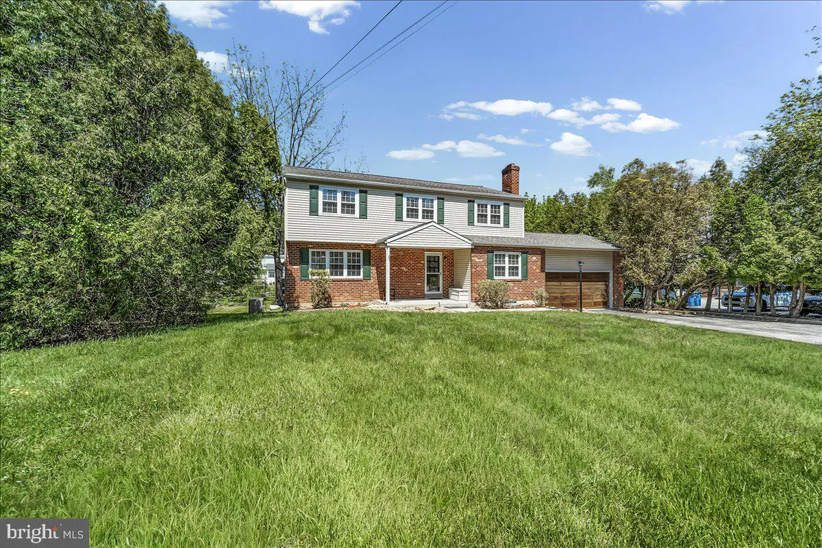 Two-story house with brick and siding, green shutters, and a large lawn under a blue sky.