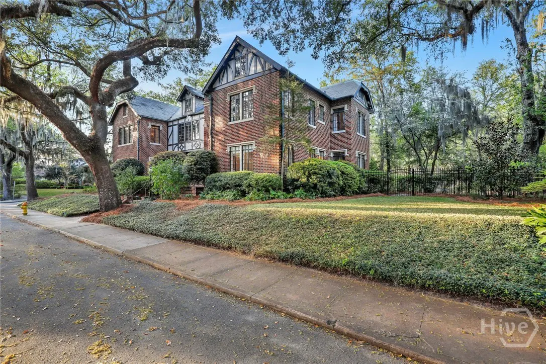 A two-story brick house with black trim and a gray roof sits on a lush green lawn with trees.