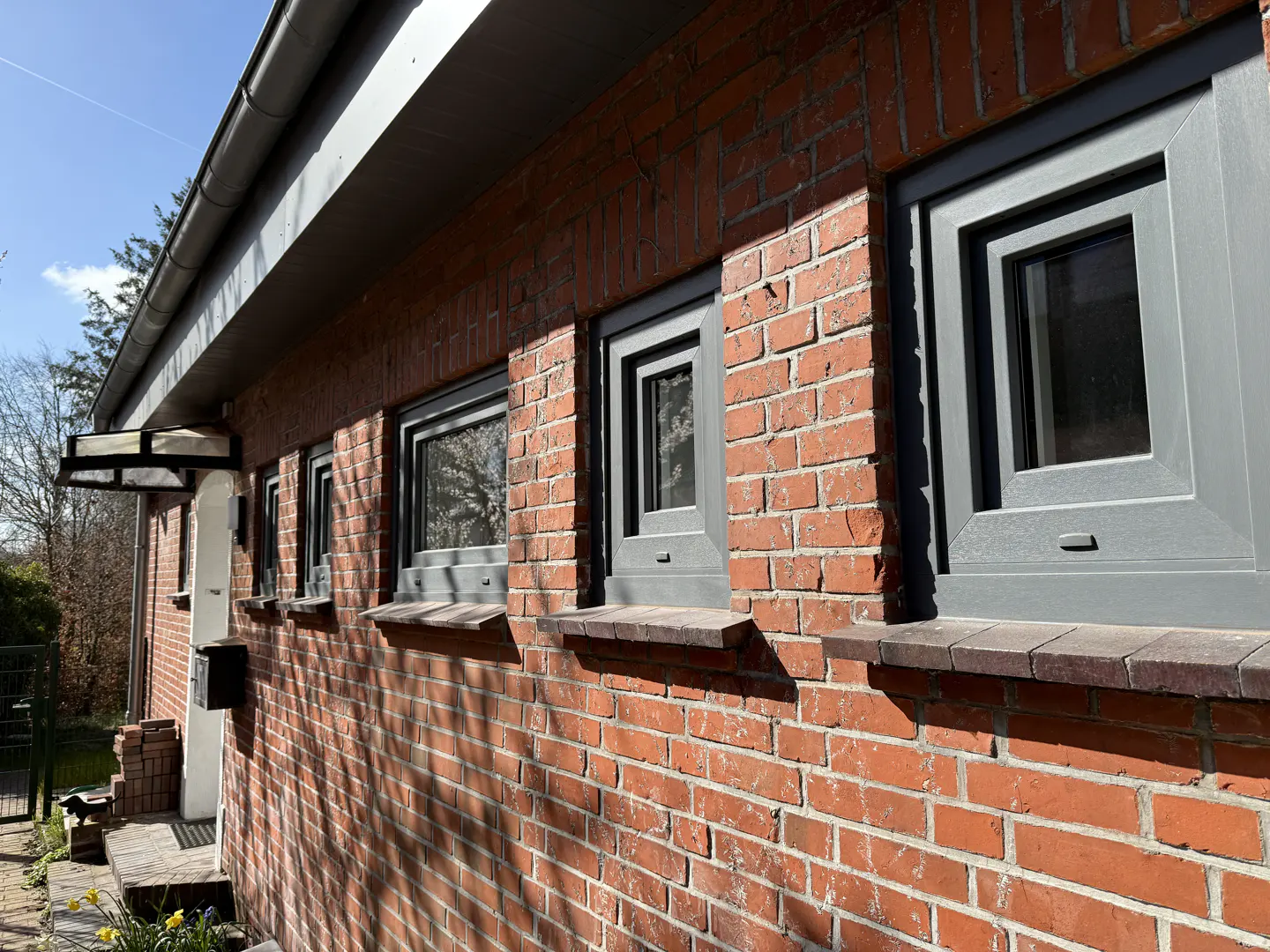 Exterior view of a red brick house with gray framed windows and a gray roof on a sunny day.