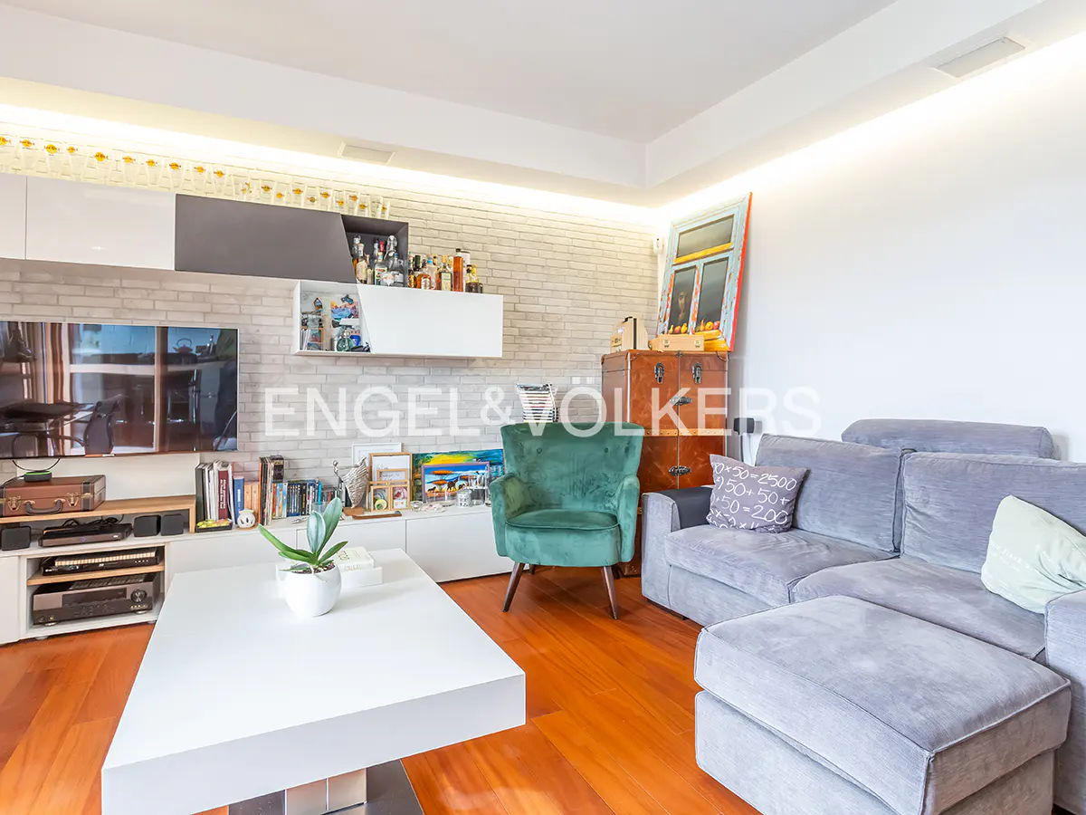 Living room with a gray sofa, green armchair, and white coffee table on a wood floor. A TV and shelves are on the wall.