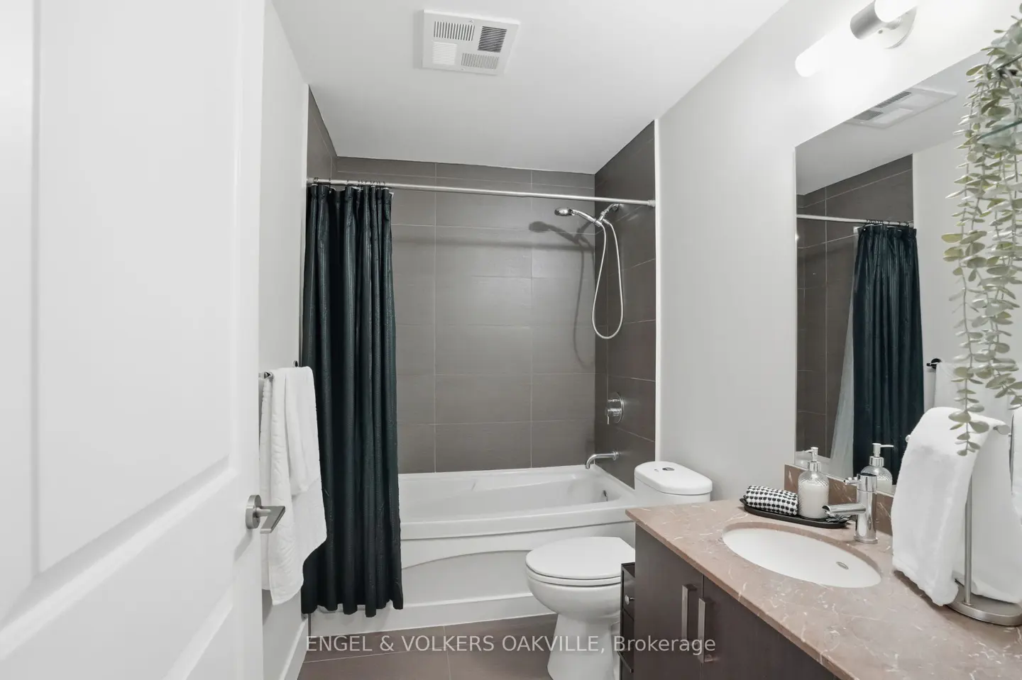 Bathroom with gray tile, white tub, and dark green shower curtain. A brown vanity with a white sink is on the right.