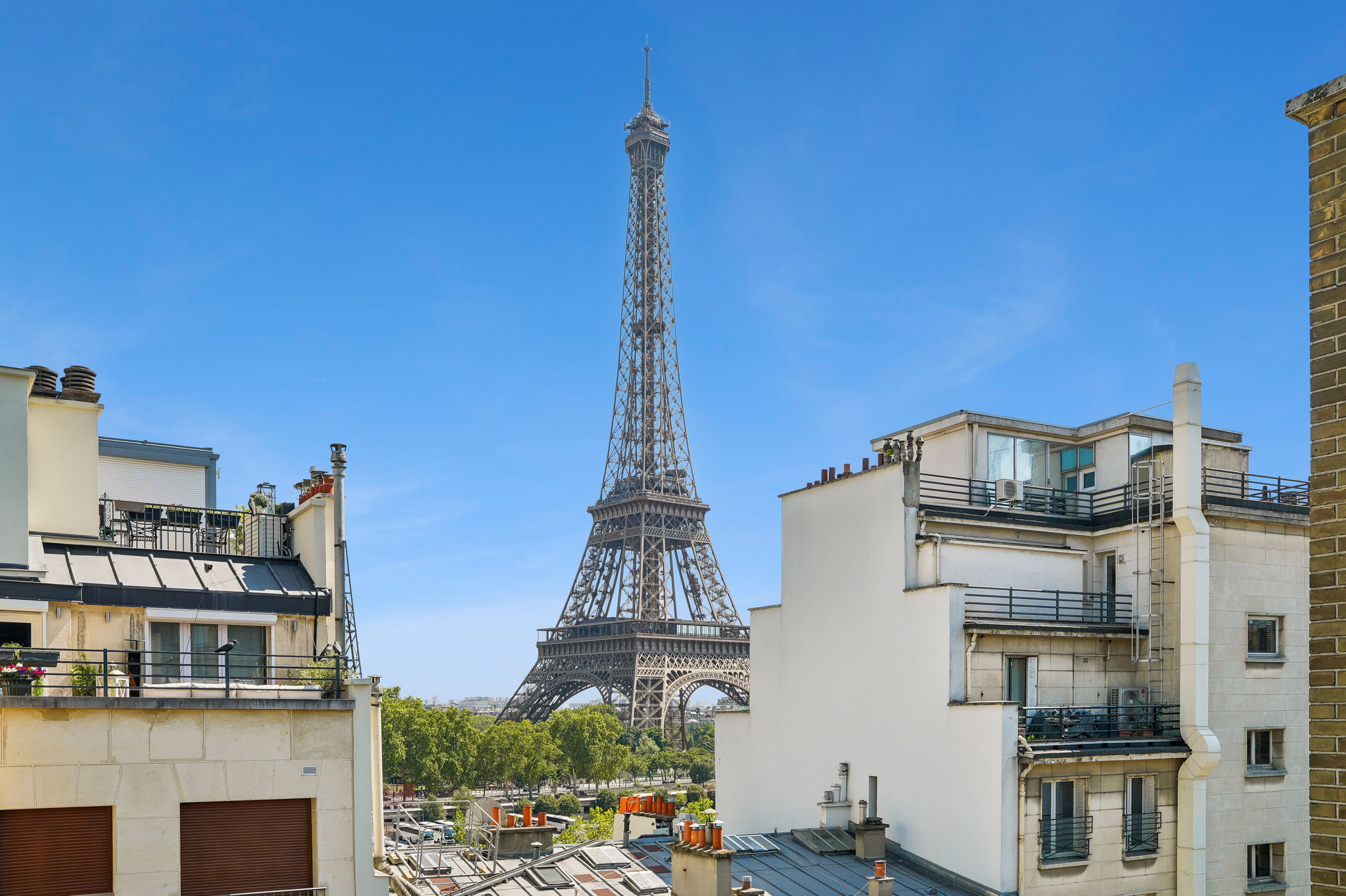 View of the Eiffel Tower rising above Parisian apartment buildings under a clear blue sky.