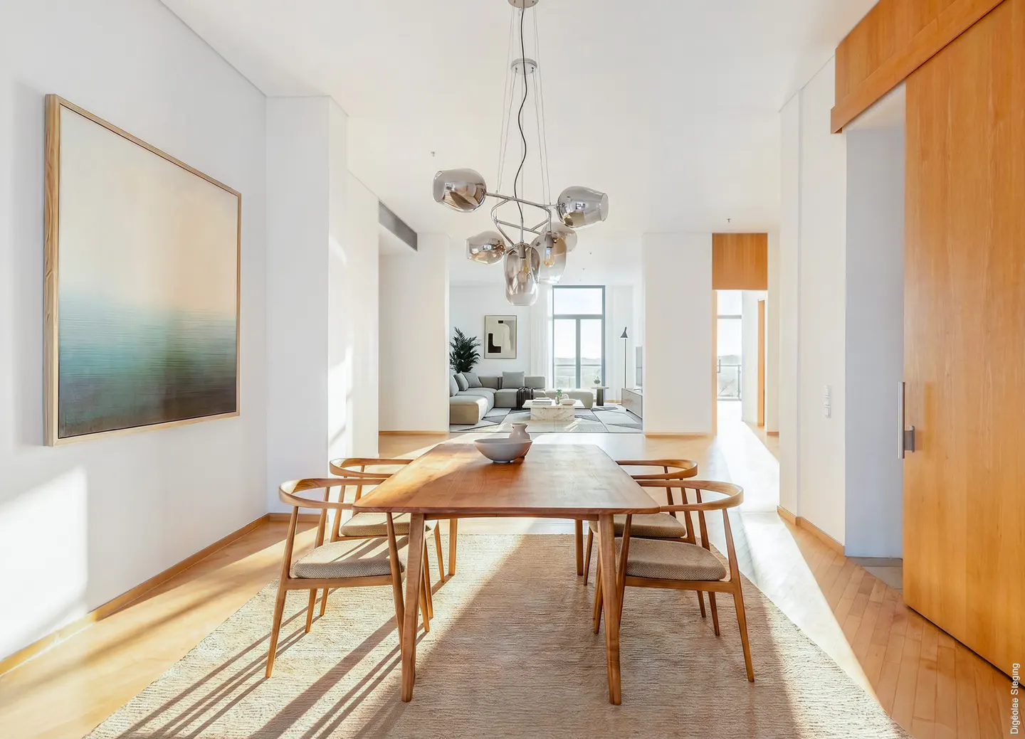 Modern dining area with a wooden table, four chairs, and a unique glass chandelier, opening into a bright living room.