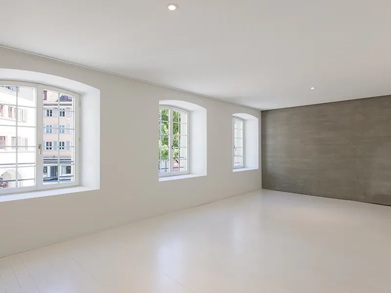 Minimalist room with white walls, white floors, three arched windows, and a textured grey accent wall.