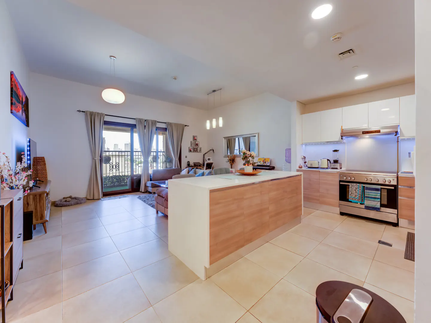 Open-concept apartment with tile floors, a kitchen island, white cabinets, and a living room with a balcony overlooking a city.
