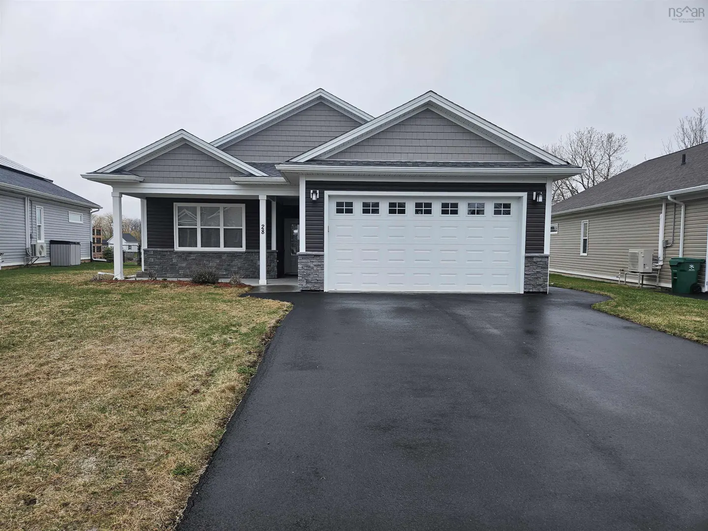 A single-story house with gray siding, a white garage door, and a black asphalt driveway.