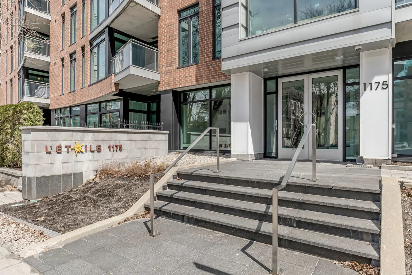 Exterior view of "L'Étoile 1175" building entrance with stone steps, metal railings, and glass doors. Brick and modern facade visible.