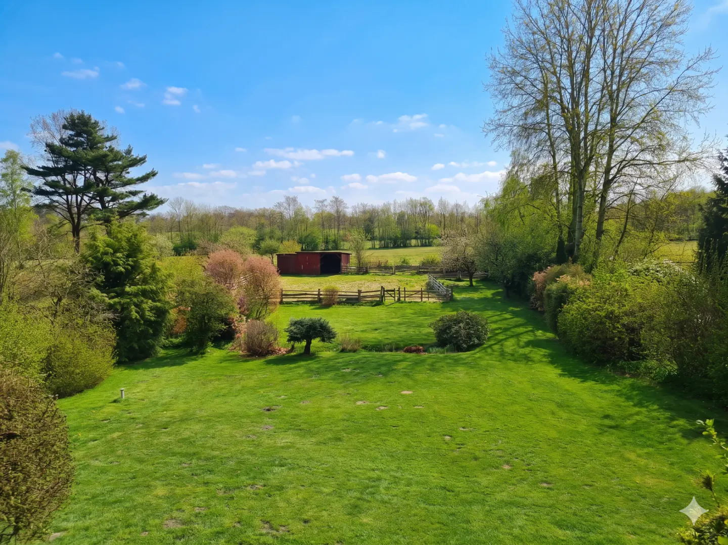 A wide shot of a green lawn with trees, bushes, and a red barn under a blue sky.