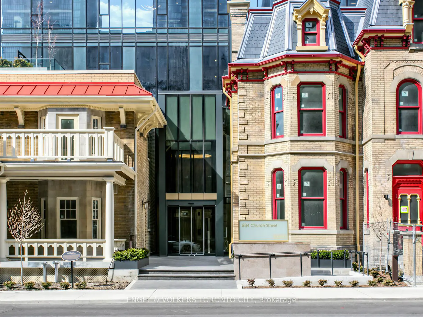 Exterior view of 534 Church Street, Toronto. A modern glass building is flanked by two historic brick buildings with red trim.