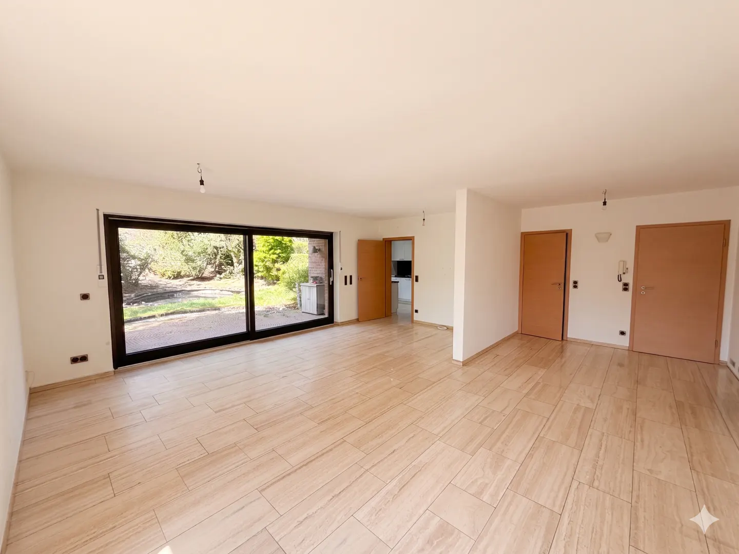 Bright, empty room with light wood-look tile flooring, white walls, and a large sliding glass door to the backyard. Two wood doors are on the right.