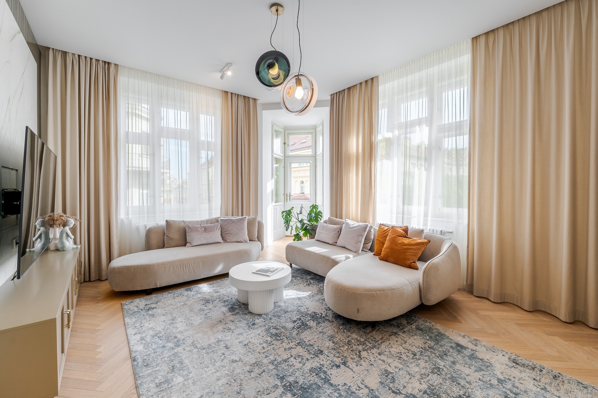 Modern living room with two beige curved sofas, a white coffee table, and a grey patterned rug under beige curtains. [AI-generated text]