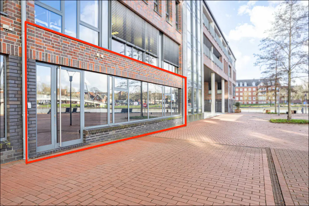 Exterior of a brick commercial building with large windows and a glass door, outlined in red. A brick walkway leads to the entrance.