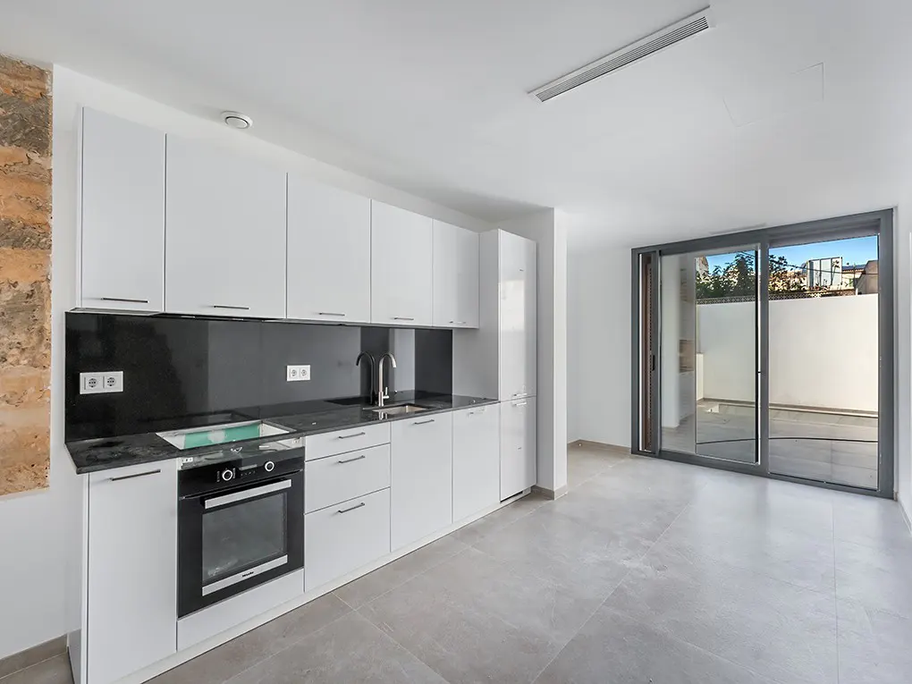 A modern kitchen with white cabinets, black countertops, and stainless steel appliances. Sliding glass doors lead to an outdoor patio.
