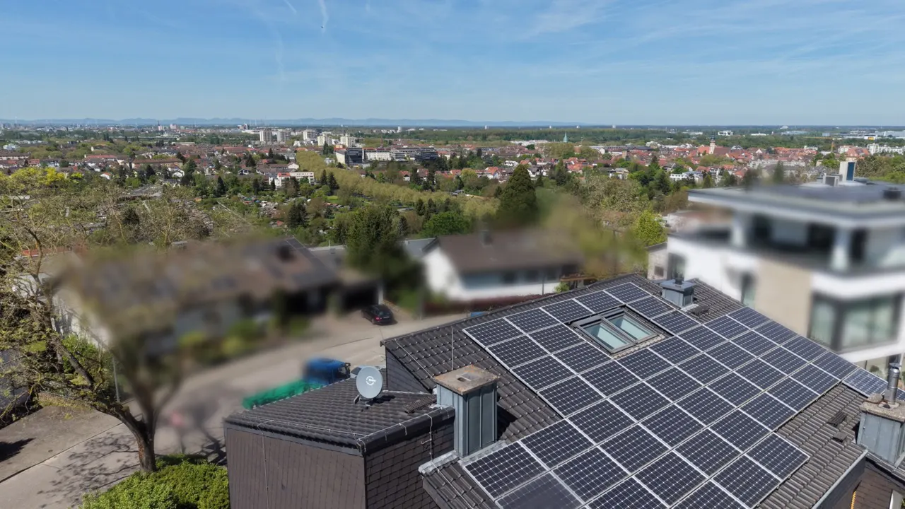 High-angle view of a dark tiled roof covered in solar panels, overlooking a suburban neighborhood under a clear blue sky.