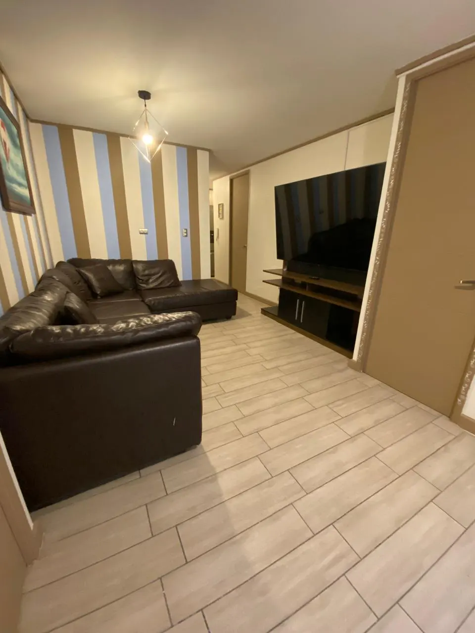 Living room with brown leather sectional sofa, TV, and striped wall. Light wood-look tile flooring.