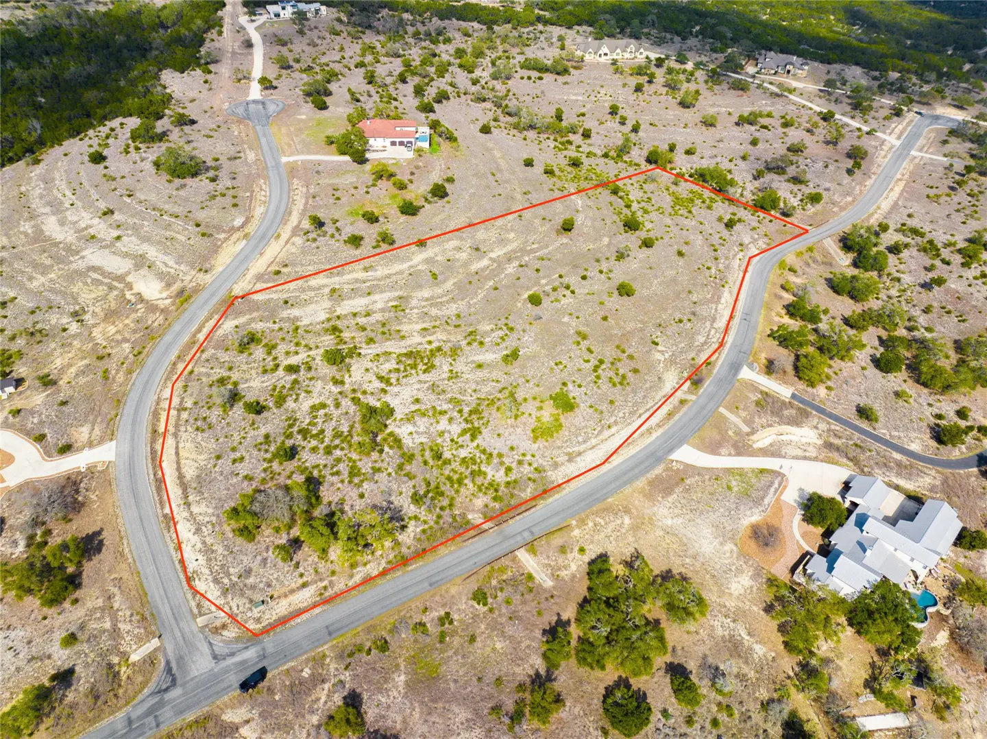 Aerial view of a vacant lot outlined in red, surrounded by roads, trees, and houses in a rural area.
