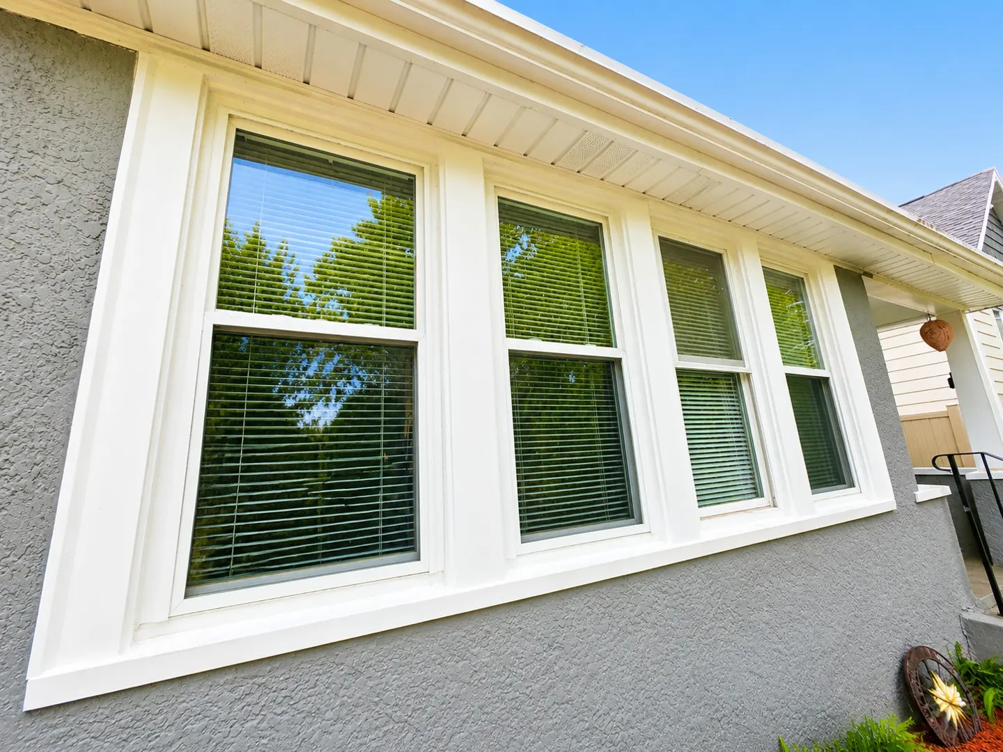 Exterior view of a house with gray stucco walls and white-framed windows with blinds.