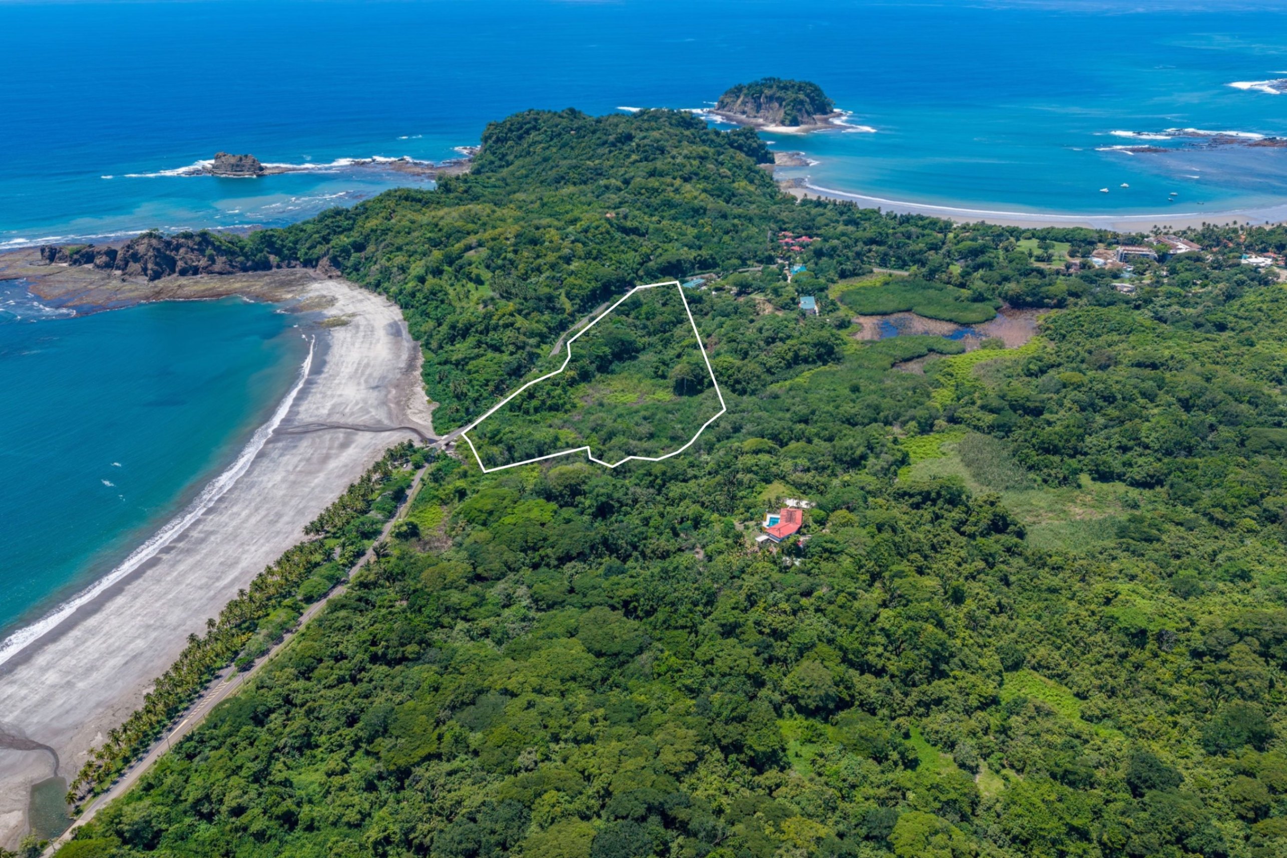 Aerial view of a coastal property outlined in white, surrounded by lush green forest, a sandy beach, and the blue ocean. [AI-generated text]