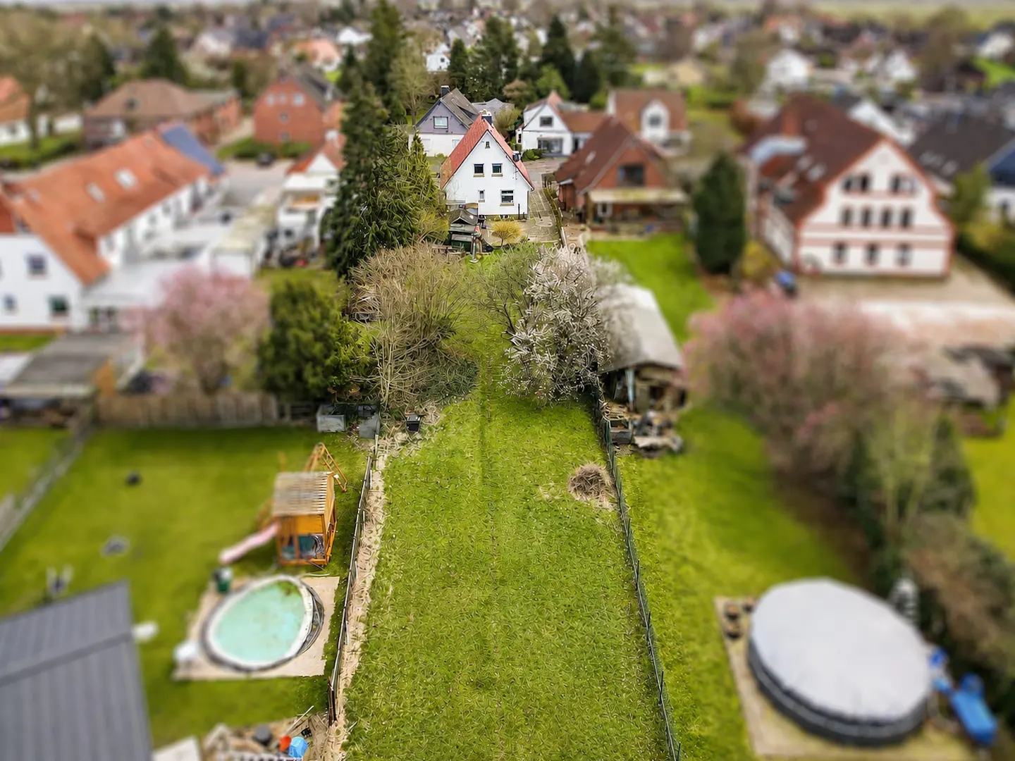 Aerial view of a green lawn with a playset, pool, and houses in the background.