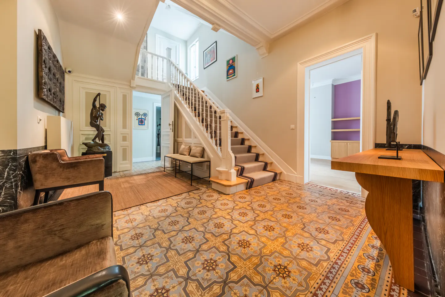 A grand foyer with patterned tile floors, a staircase with a runner, and elegant furniture.