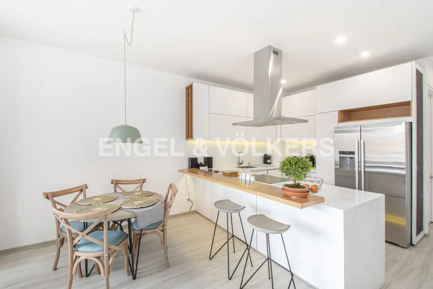 Bright, modern kitchen with white cabinets, stainless steel appliances, and a wood-topped island with gray stools. A round dining table sits nearby.
