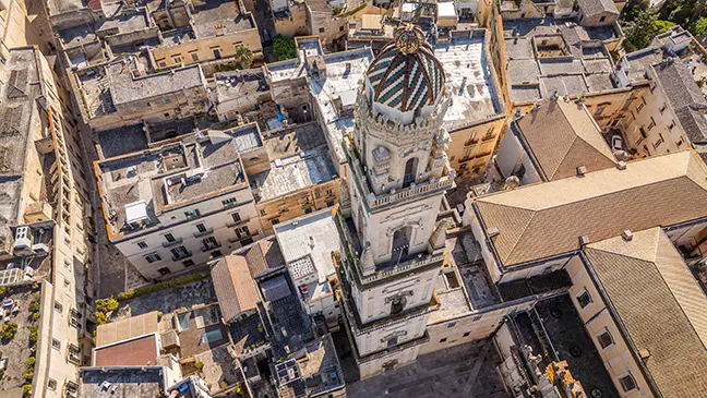 Aerial view of a city with beige buildings and a tall church tower with a green and white tiled dome.
