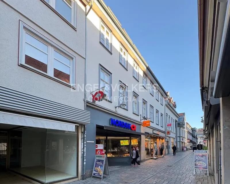Street view of a European city with shops and apartments. Cobblestone street, blue sky, and people walking.