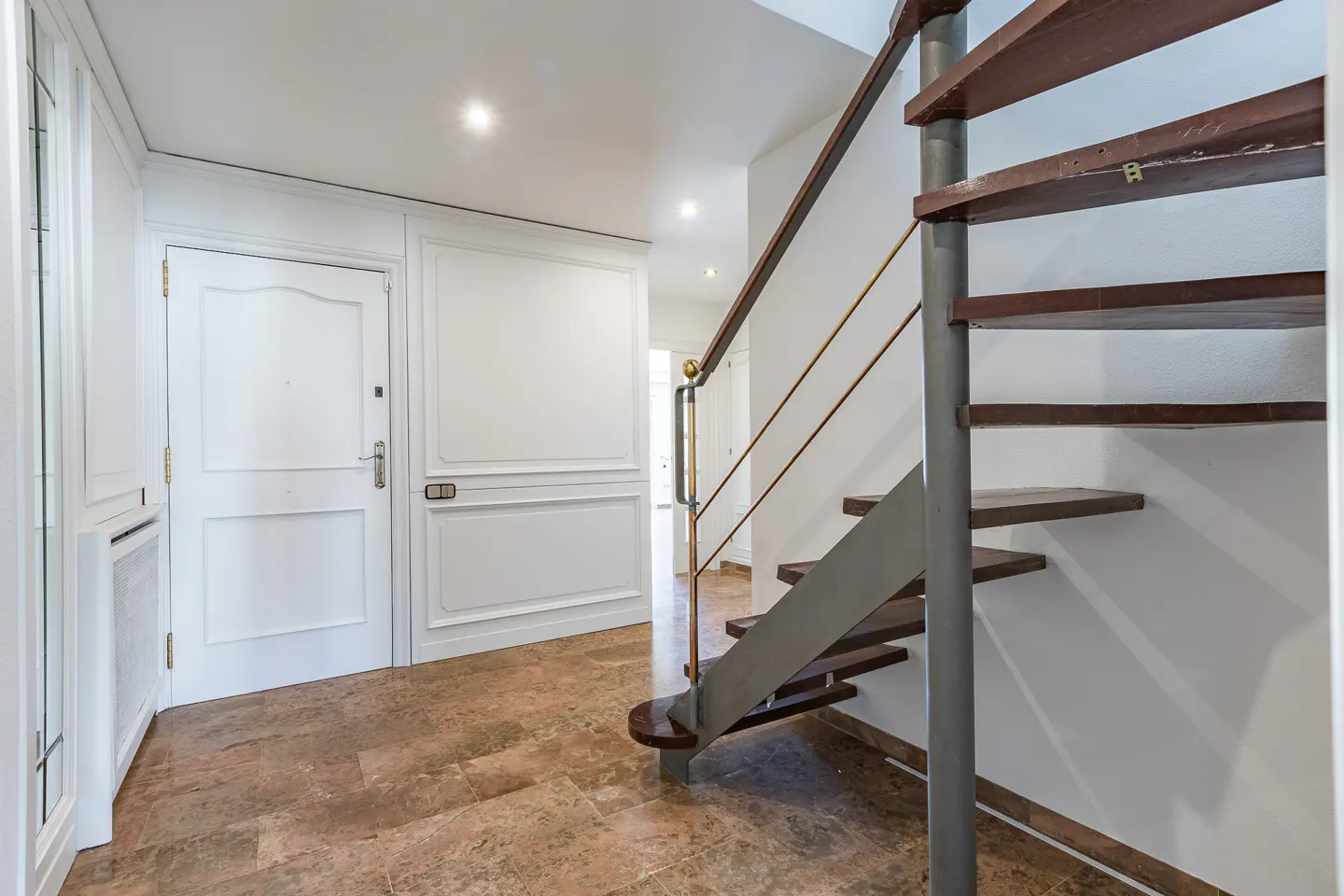 Entryway with a white door, marble floors, and a spiral staircase with wooden steps and metal railings.