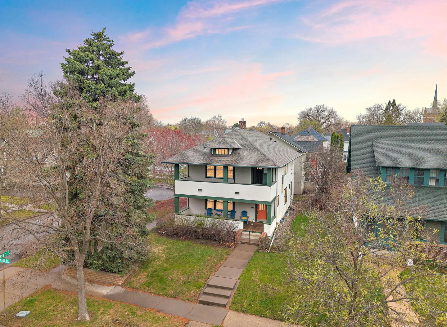 Two-story white house with green trim, a gray roof, and an orange door, viewed from above. A sidewalk leads to the house.