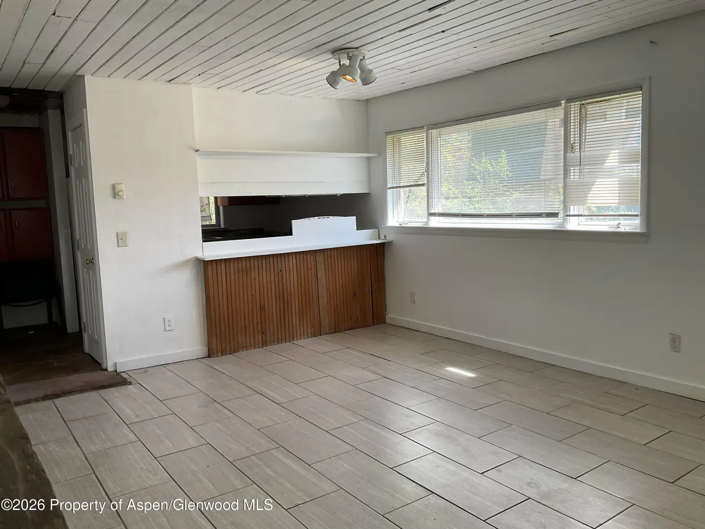 A bright room with white walls, a wood-paneled half wall, and a window with blinds. The floor is tiled.