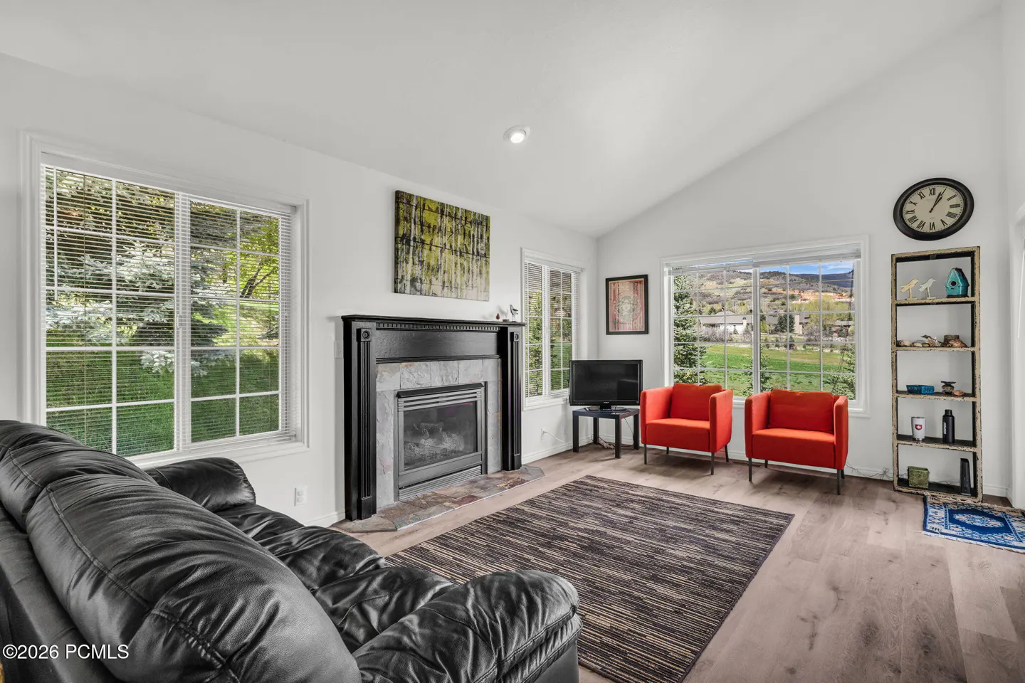 Living room with black leather sofa, fireplace, two orange chairs, and large windows with views.