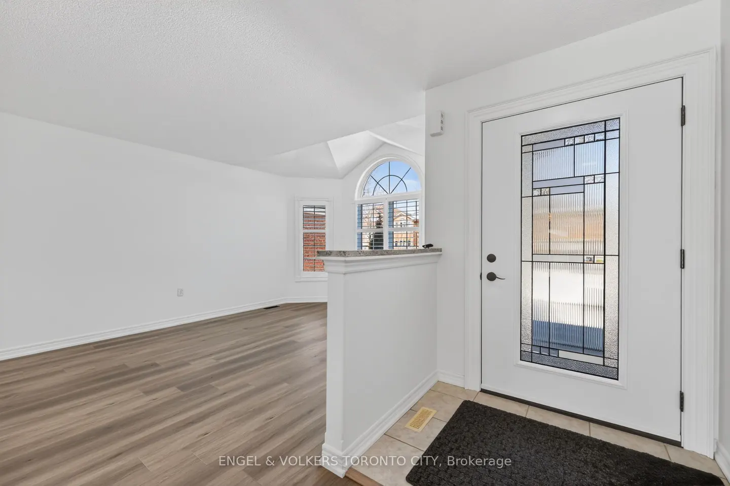 Bright entryway with white walls, light wood floors, and a decorative glass front door. A half wall separates the entry from the living area.