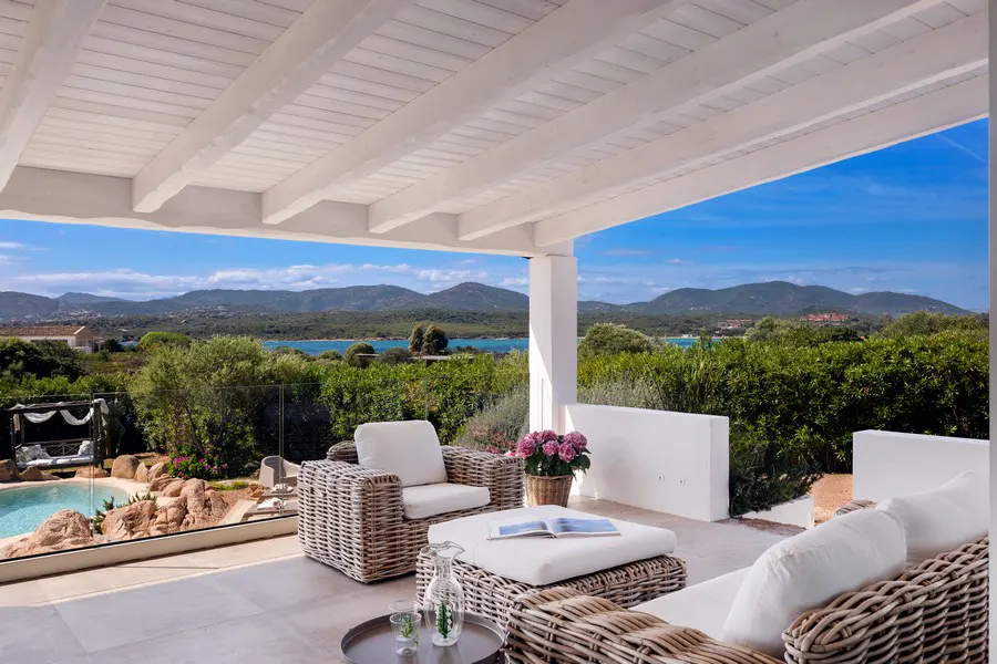 Outdoor patio with wicker furniture, white cushions, and a view of the ocean and mountains.
