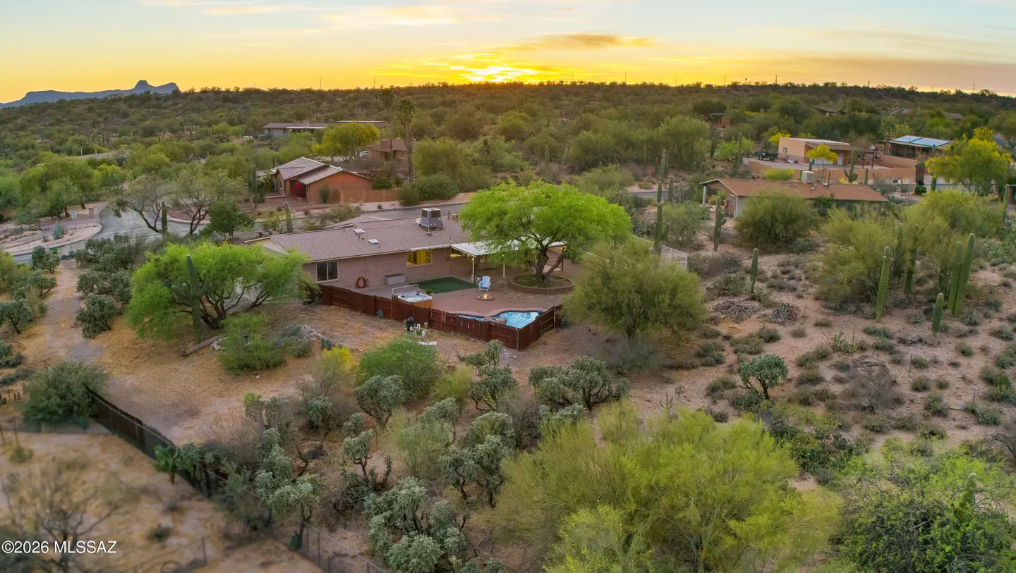 Aerial view of a tan ranch-style house with a pool and desert landscaping at sunset.