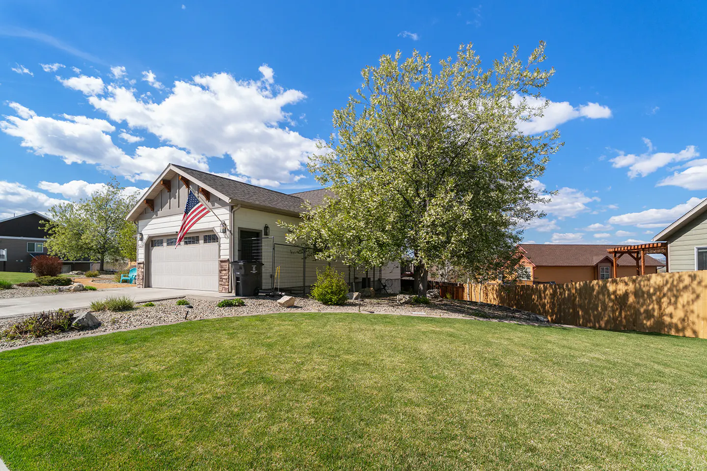 A single-story house with a green lawn, a tree, and an American flag on a sunny day.