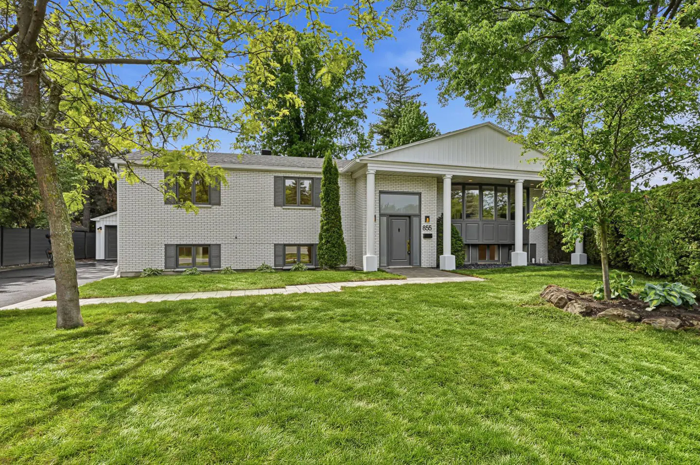 White brick ranch house with a covered porch, gray shutters, and a well-manicured lawn under a bright blue sky.