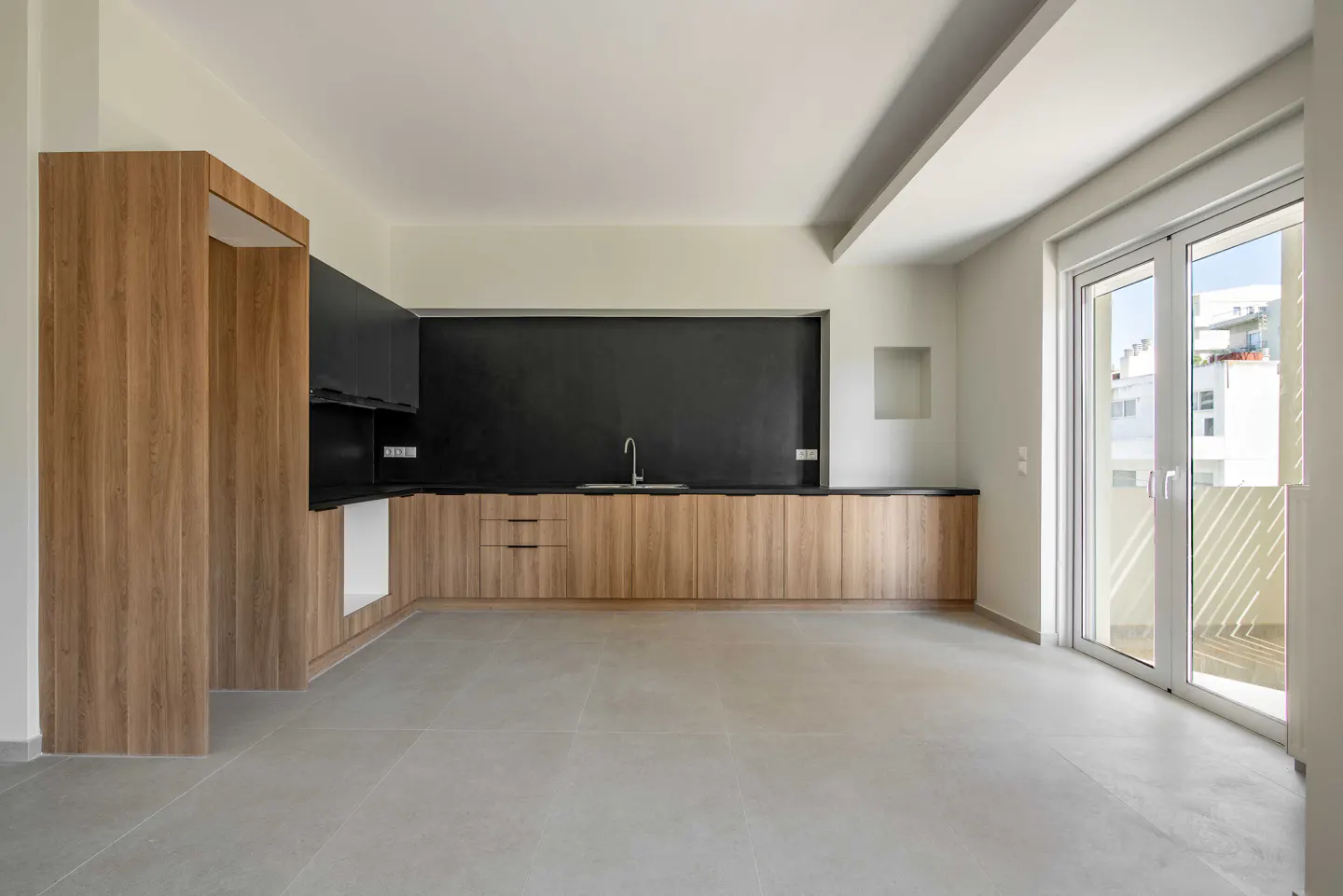 Bright, empty kitchen with wood cabinets, black backsplash, and gray floors. Glass doors lead to a balcony.