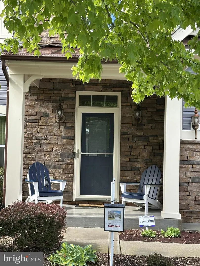 Front porch view of a stone house with two blue Adirondack chairs and a blue front door.