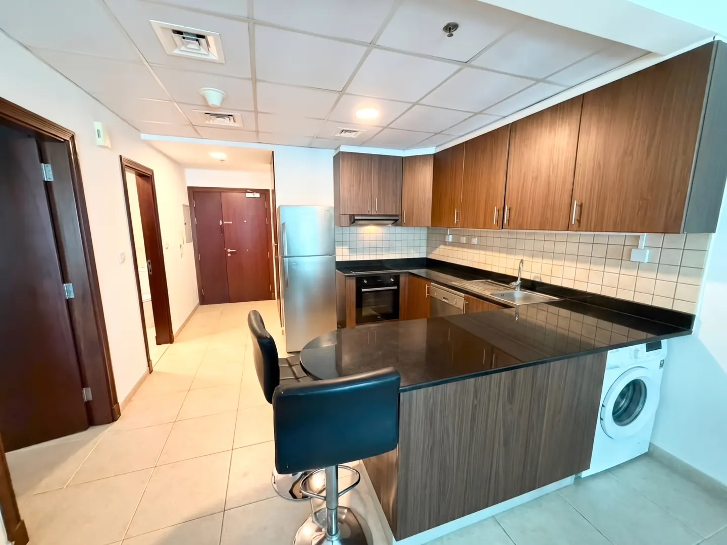 Modern kitchen with wood cabinets, black countertops, stainless steel appliances, and a breakfast bar with two stools.