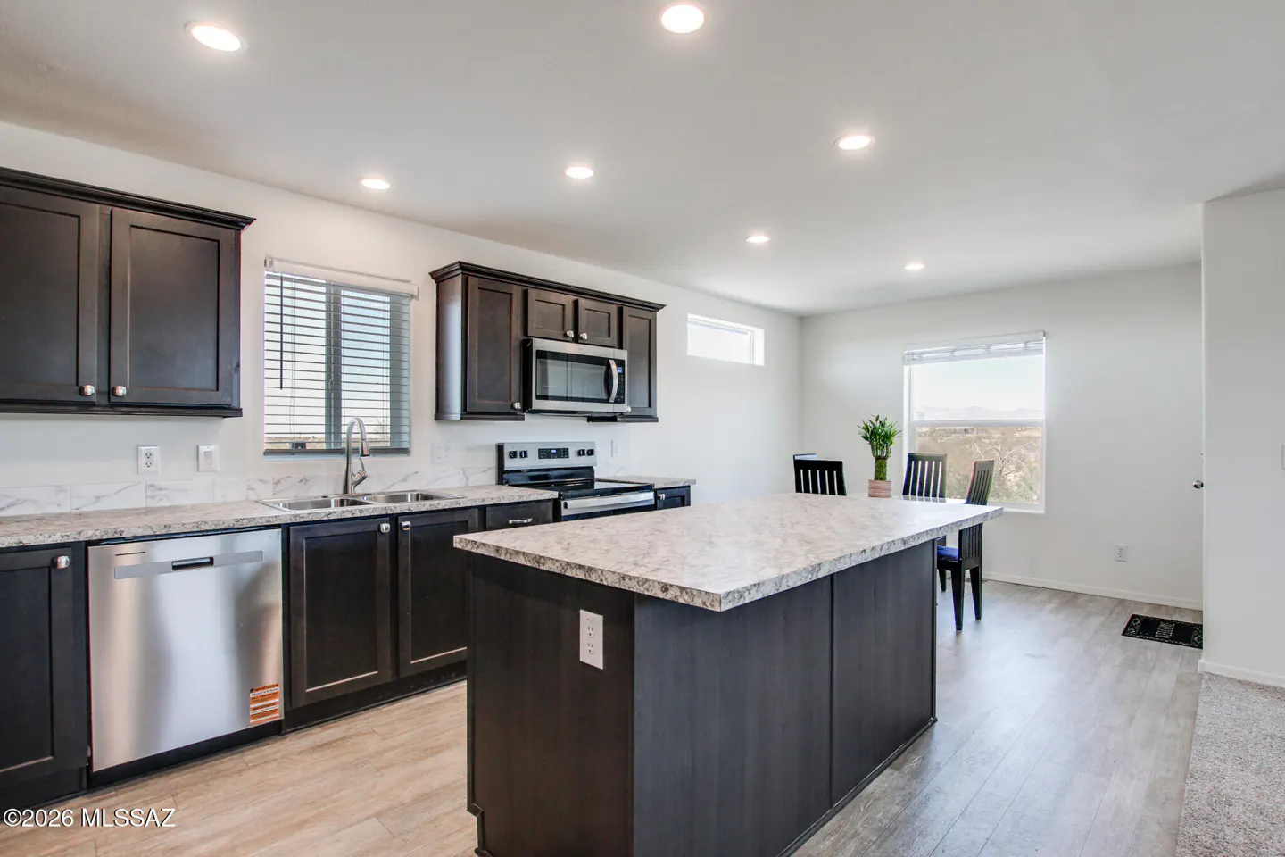 Bright kitchen with dark cabinets, stainless steel appliances, and a large island with a light countertop. A dining table sits near a window.
