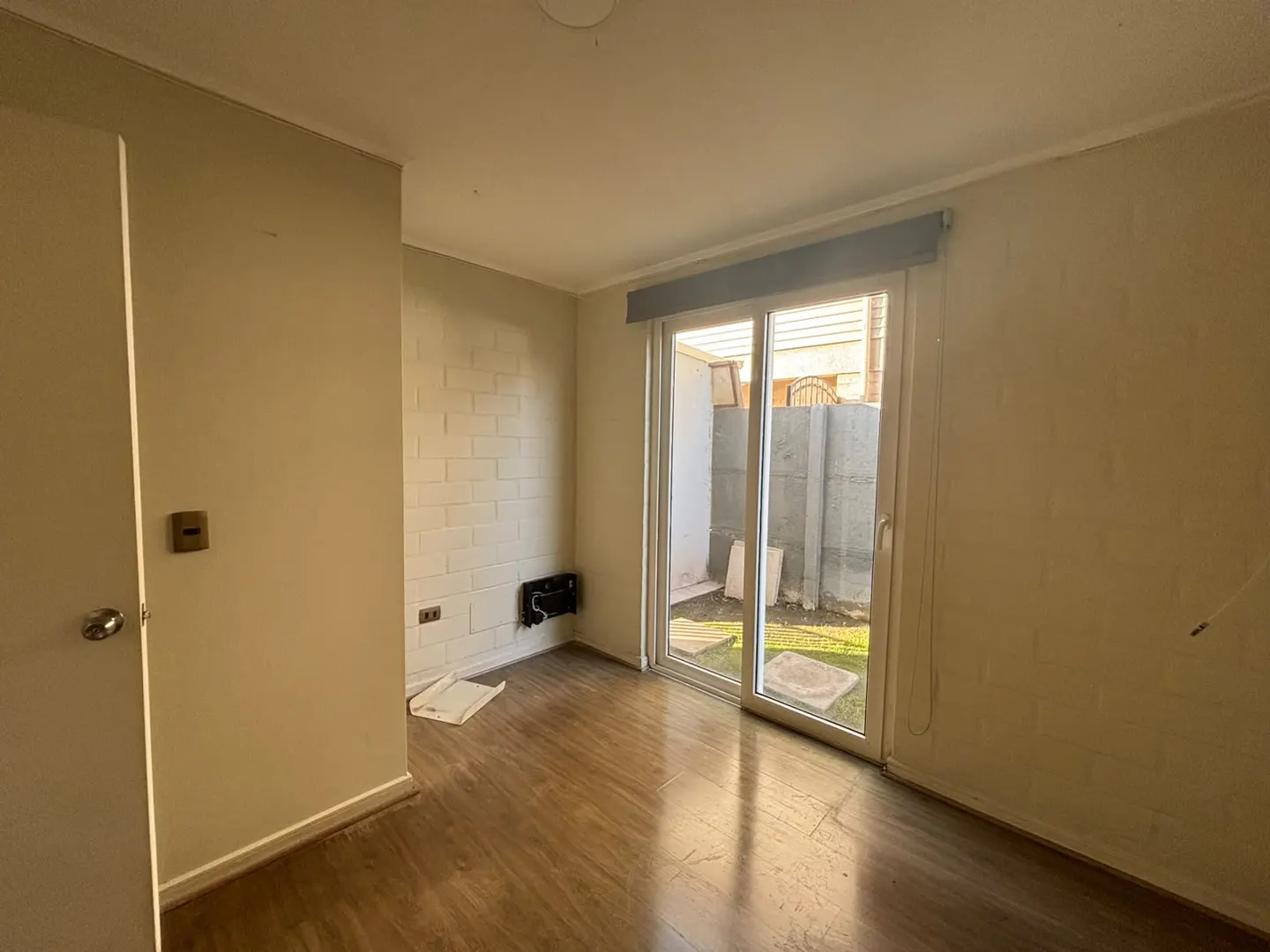 Empty room with light-colored brick walls, wood-look flooring, and sliding glass doors leading to a small backyard.