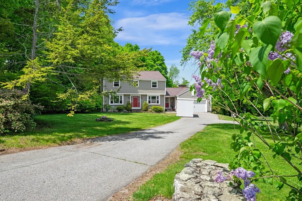 Two-story gray house with a red door and white garage, surrounded by green trees and grass.